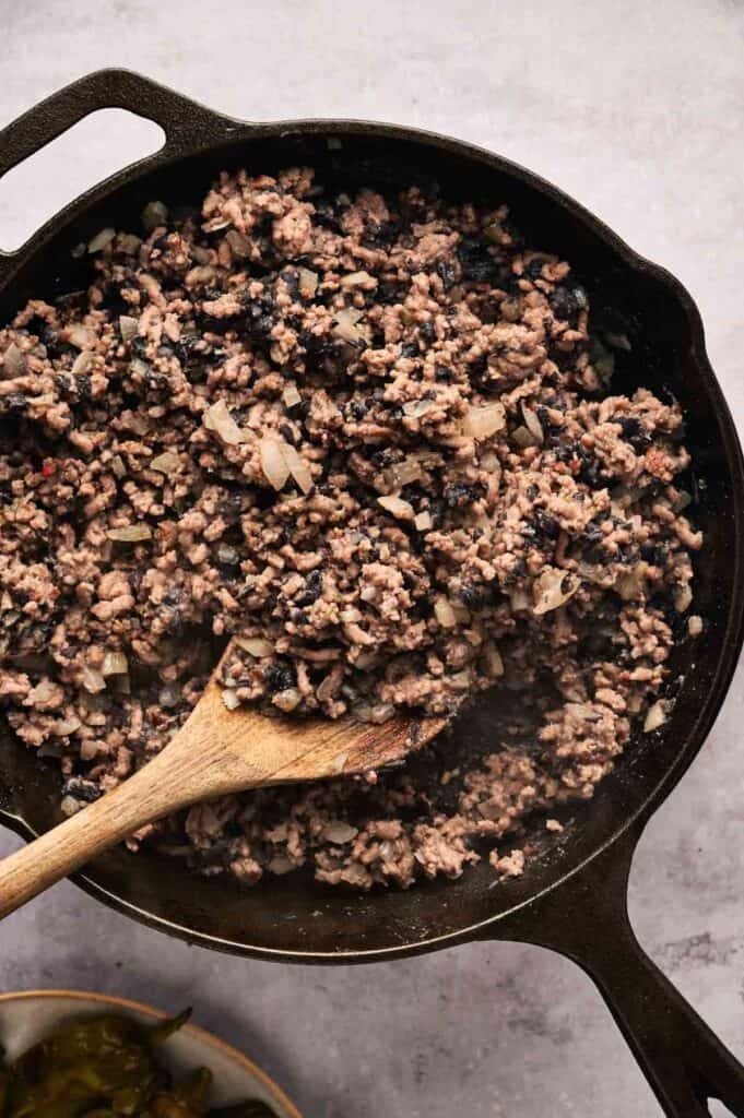 Cooked ground meat with finely chopped onions and mushrooms in a cast-iron skillet, stirred with a wooden spoon, is the perfect base for a chili relleno casserole twist.