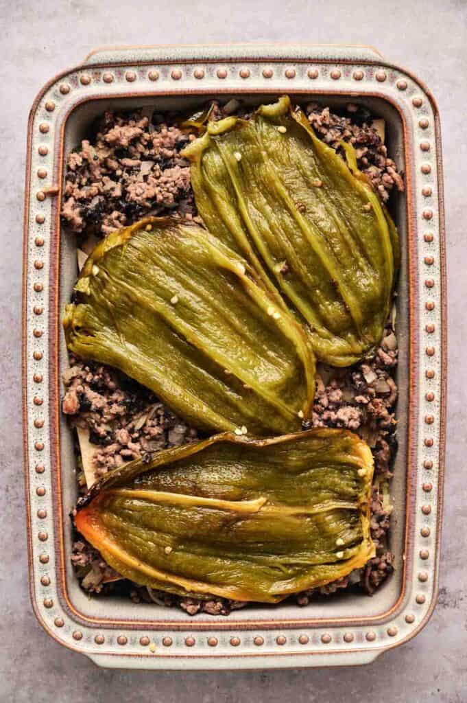 Baking dish with a delicious chili relleno casserole featuring three roasted green chili peppers on top of savory ground meat and black beans.
