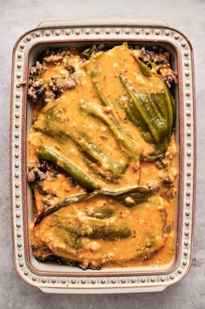A baking dish brims with a delicious chili relleno casserole, featuring roasted green chiles, ground meat, and melted cheese nestled in a creamy sauce.