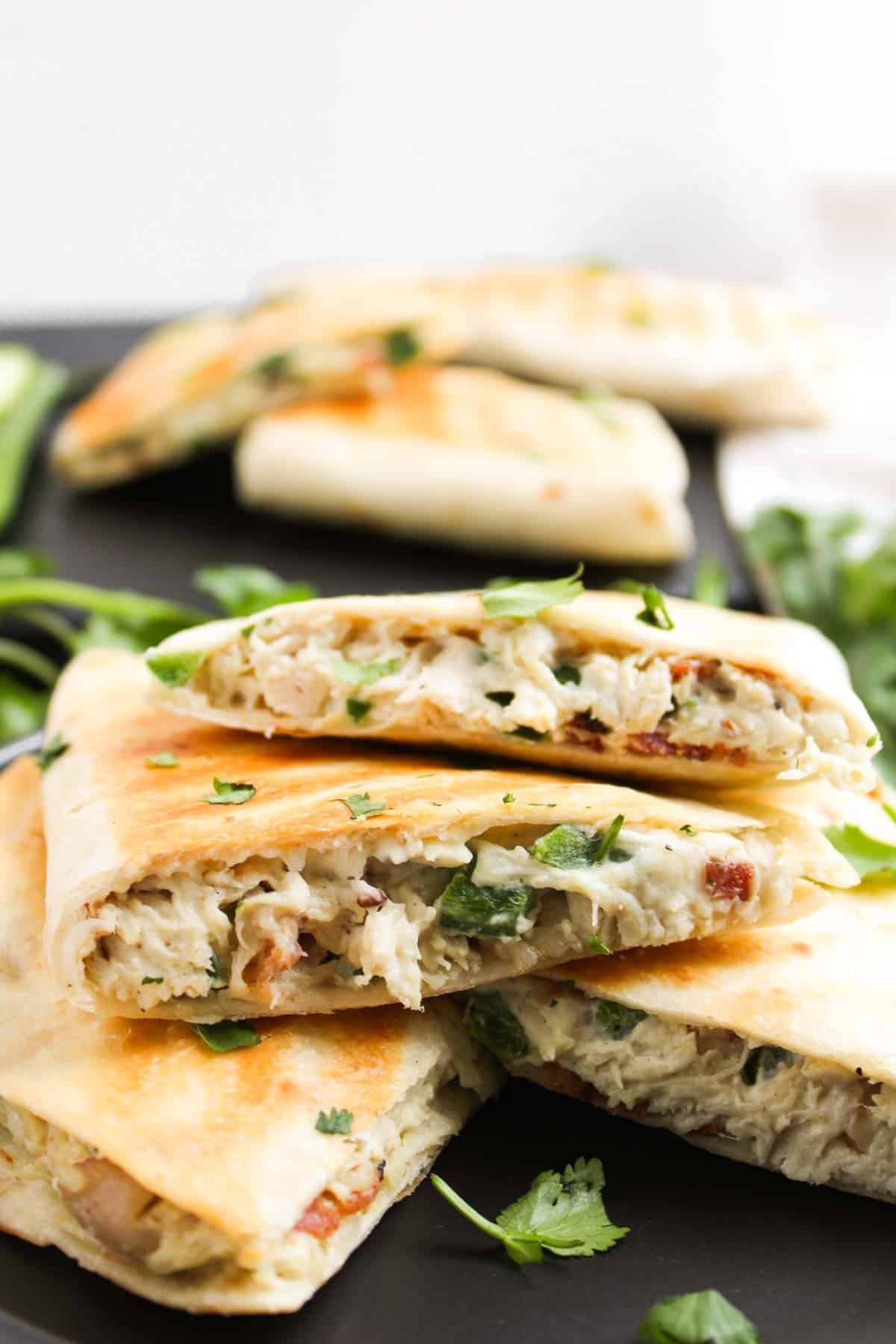 Jalapeño Popper Chicken Quesadillas slices filled with a creamy chicken mixture and fresh herbs, arranged on a dark plate.