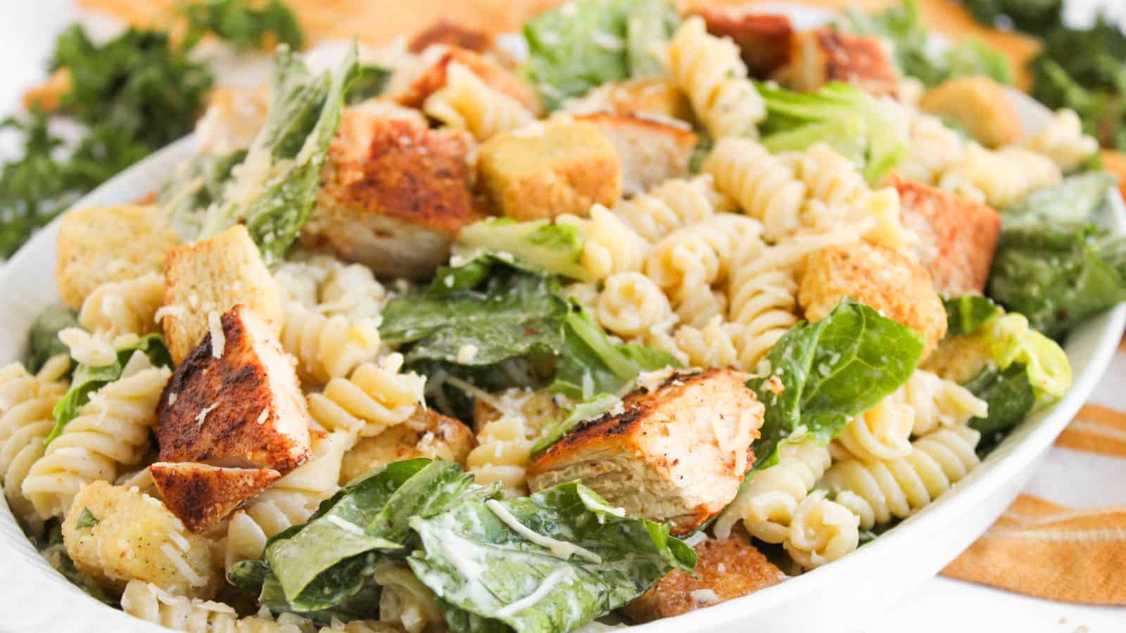 A plate of pasta salad with grilled chicken pieces, romaine lettuce, croutons, and creamy dressing.
