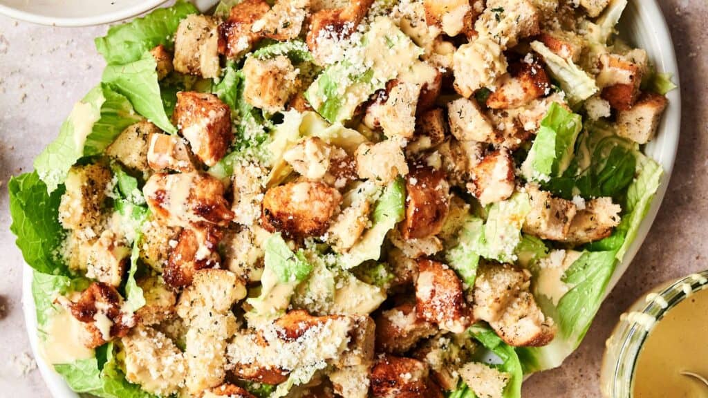 A Caesar salad with chopped grilled chicken, croutons, grated cheese on romaine lettuce, served with dressing on the side.