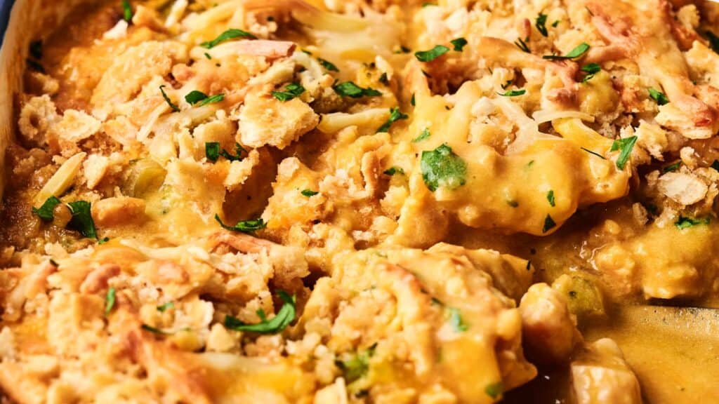 Close-up of a baked cheesy chicken casserole topped with herbs and crushed crackers.