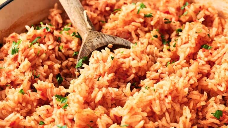 A close-up of cooked Mexican rice with a wooden spoon, garnished with chopped parsley.