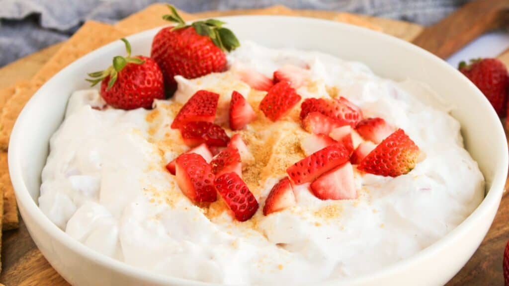 A bowl filled with creamy cheesecake dip, topped with sliced fresh strawberries and a light sprinkle of crumbs.