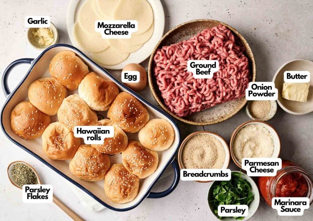 Various labeled ingredients for Air Fryer Meatball Sliders are laid out, including Hawaiian rolls, ground beef, mozzarella, parsley, egg, garlic, butter, breadcrumbs, Parmesan, onion powder, and marinara sauce.
