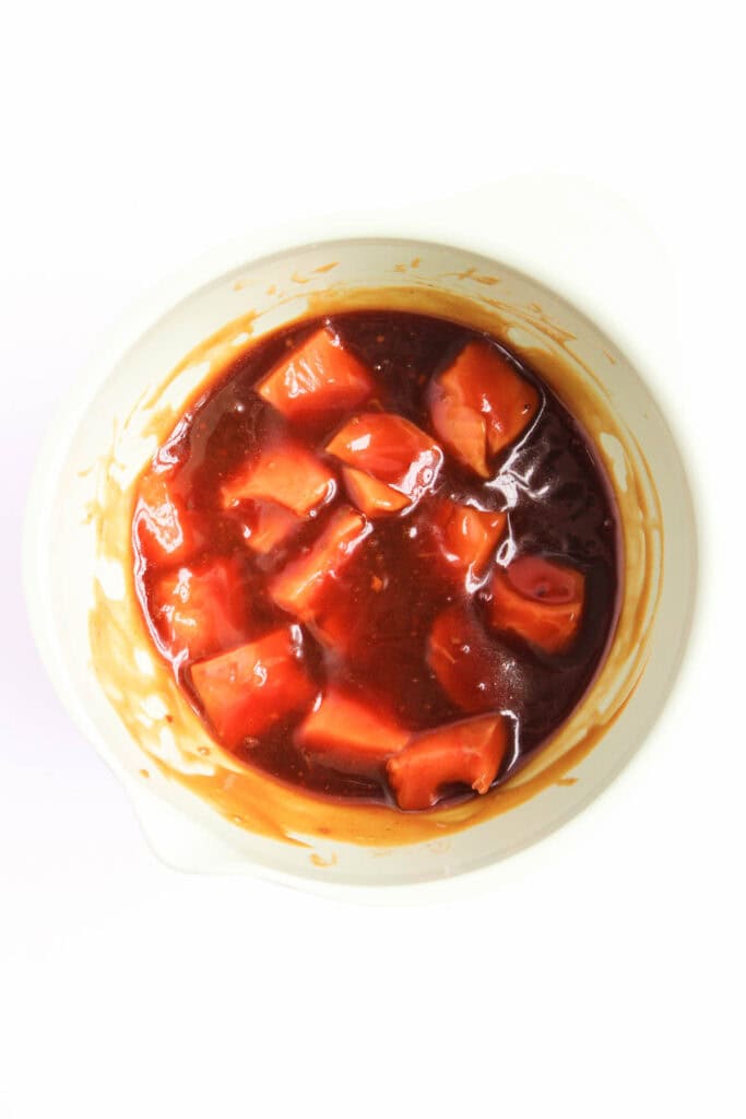 A white mixing bowl contains diced pieces of red fruit or vegetable in a dark teriyaki sauce, reminiscent of a vibrant Teriyaki Salmon Bowl.