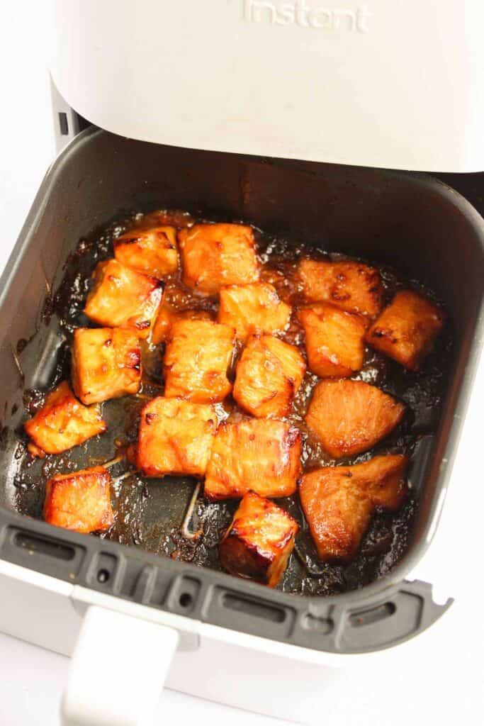 Chunks of glazed tofu sizzling in a white air fryer basket bring the vibrant flavors of an Asian-inspired Teriyaki Salmon Bowl to mind.