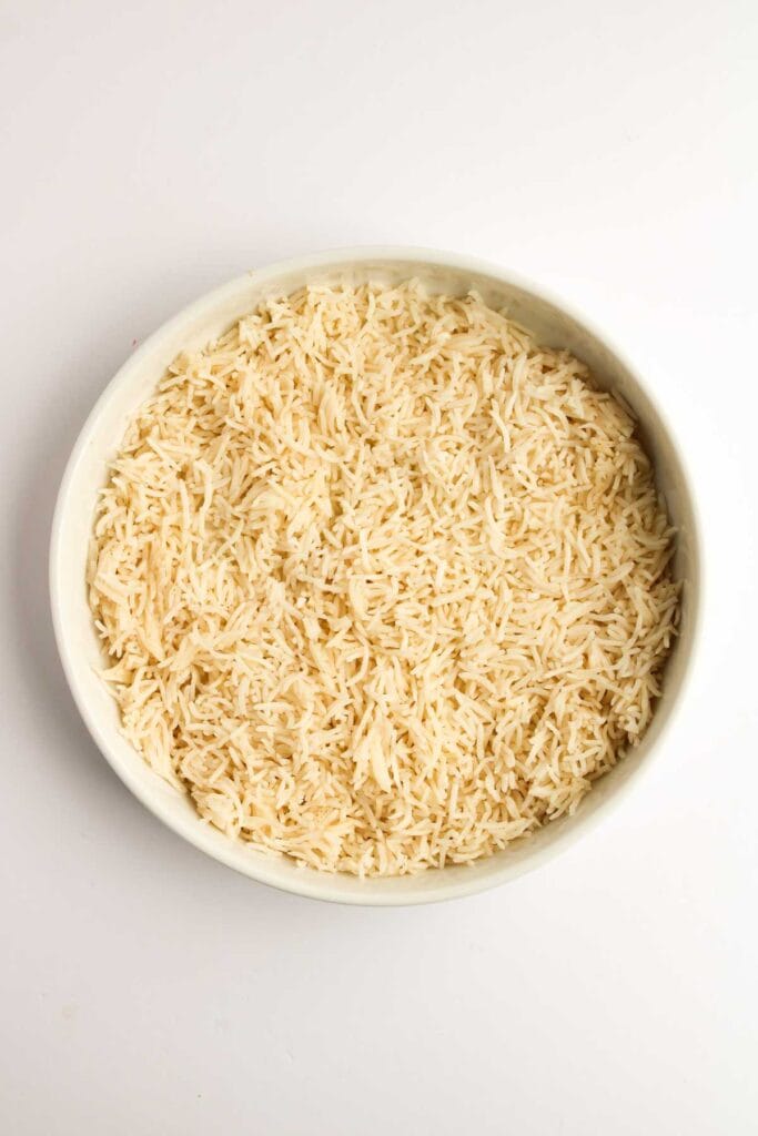 A bowl of fragrant basmati rice, perfectly complementing the vibrant colors and rich flavors of a Teriyaki Salmon Bowl, rests invitingly on a pristine white surface.