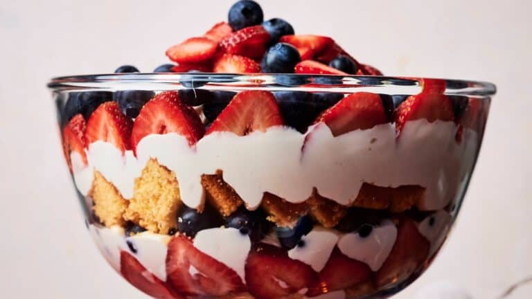 A glass trifle bowl filled with layered strawberries, blueberries, whipped cream, and sponge cake.