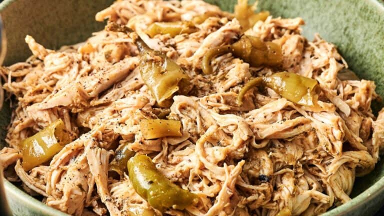 Shredded chicken with pepper slices and spices served in a green bowl.
