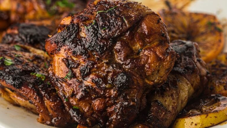 Close-up of charred, grilled meat garnished with herbs, served alongside roasted potatoes on a white plate.