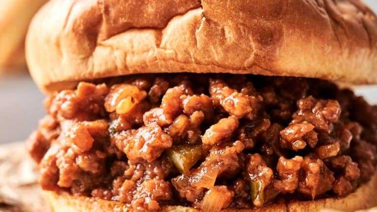 Close-up of a sloppy joe sandwich with seasoned ground meat and sauce served in a toasted hamburger bun.