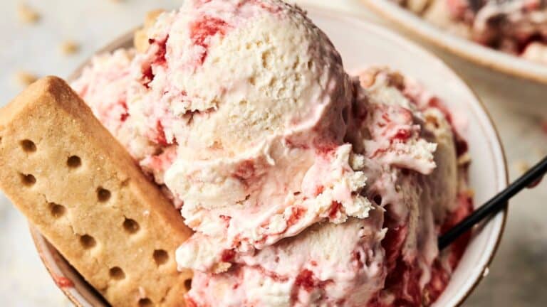 A bowl of strawberry swirl ice cream with a rectangular shortbread cookie and a spoon.