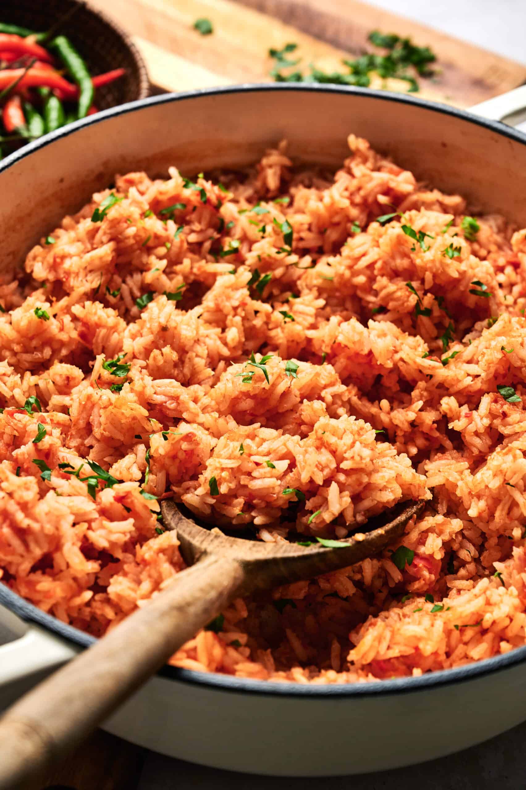 A pot of flavorful Mexican rice with a wooden spoon, garnished with chopped herbs.