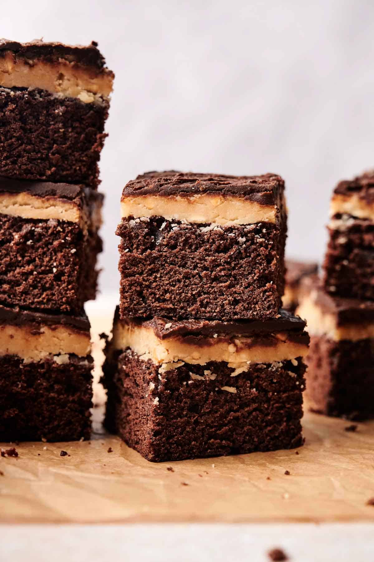 Stacked buckeye brownies with a rich peanut butter layer rest on parchment paper.
