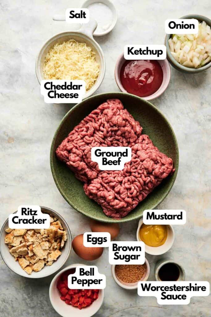 A variety of labeled ingredients for Cracker Barrel Meatloaf are displayed, including ground beef, cheddar cheese, eggs, bell pepper, onion, ketchup, mustard, brown sugar, salt, Ritz crackers, and Worcestershire sauce.