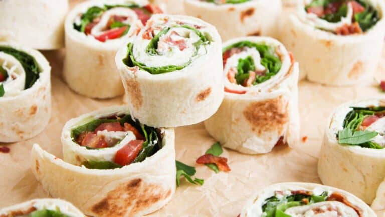 Pinwheel wraps filled with lettuce, tomato, and other vegetables arranged on parchment paper.