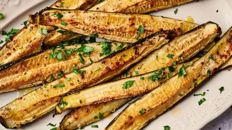 Roasted zucchini halves garnished with chopped parsley on a white plate.