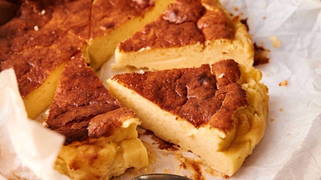 Several slices of a golden-brown, crustless cheesecake are arranged on parchment paper, revealing a creamy and dense interior.