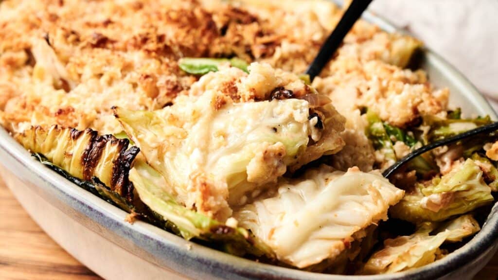 A close-up of a baked casserole dish filled with creamy cabbage gratin, with a serving spoon lifting out a portion.