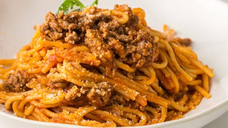 A plate of spaghetti topped with ground beef meat sauce and grated cheese, garnished with a basil leaf.