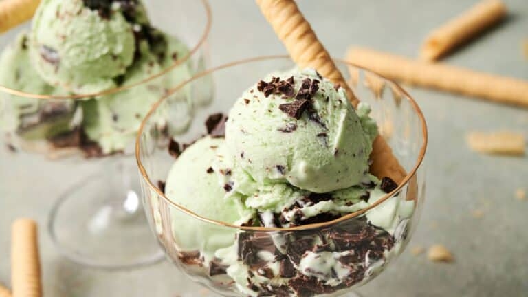 Two glass bowls filled with mint chocolate chip ice cream, topped with chocolate pieces and each served with a rolled wafer cookie.