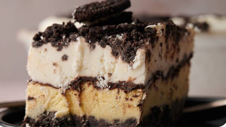 A close-up of a layered ice cream cake with chocolate cookie crumbles and two whole cookies on top, served on a plate.