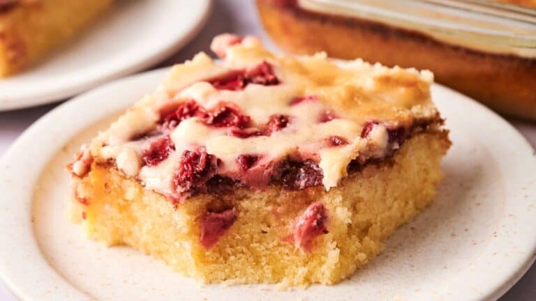 A square slice of cherry-topped cake with a golden, moist base is served on a white plate.