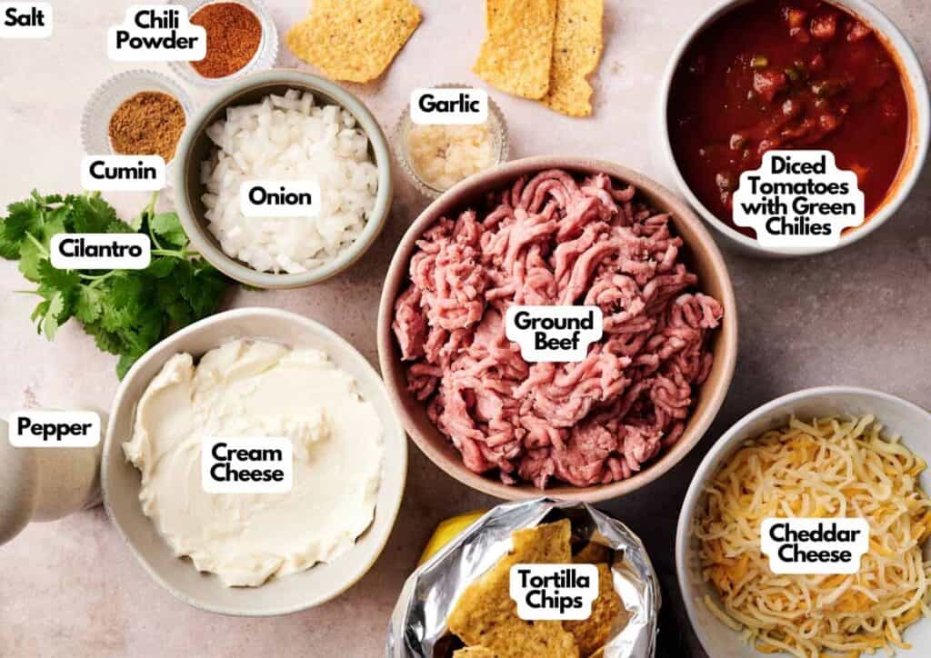 Assorted ingredients for a cowboy queso dip recipe, including ground beef, cream cheese, cheddar cheese, onion, cilantro, spices, garlic, diced tomatoes with chiles, and tortilla chips.