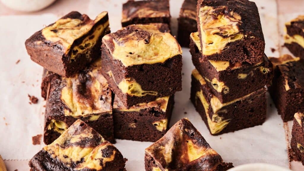 Several squares of chocolate brownies with a yellow and brown marbled pattern are stacked and arranged on parchment paper.