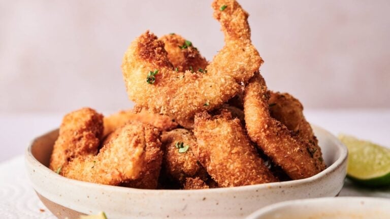 A bowl filled with golden-brown, breaded and fried shrimp garnished with chopped herbs, with a wedge of lime visible on the side.