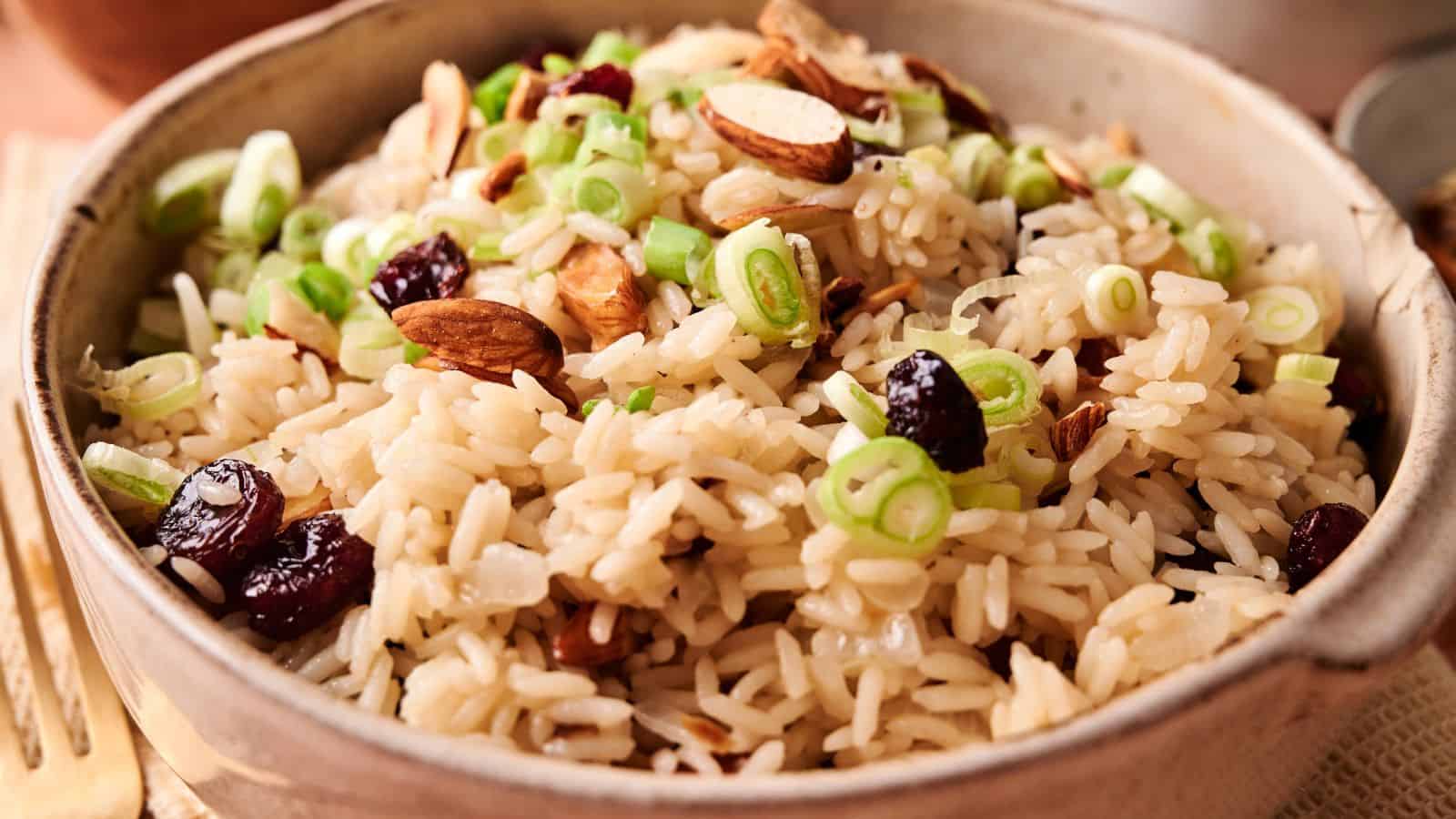 A bowl of rice pilaf topped with sliced green onions, almonds, and dried cranberries.