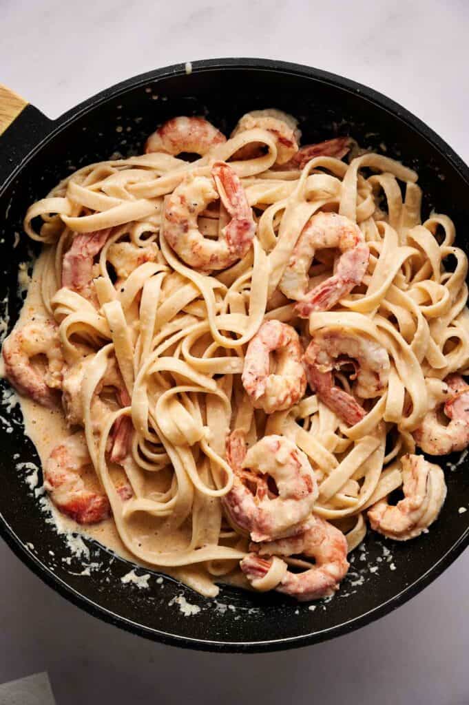 Fettuccine pasta with shrimp in a creamy sauce is served in a black skillet.