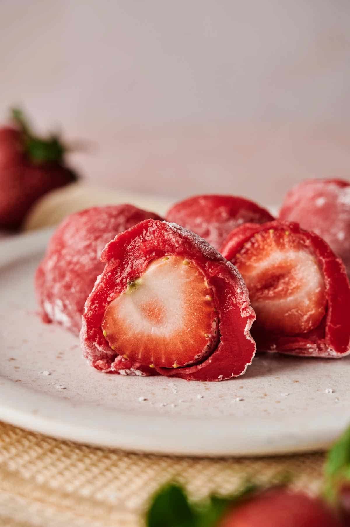 Close-up of Strawberry Mochi on a plate, showing a whole strawberry wrapped in soft red mochi dough.