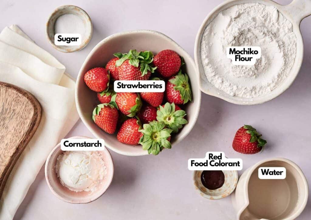 Bowls of labeled ingredients for Strawberry Mochi—strawberries, mochiko flour, sugar, cornstarch, red food colorant, and water—are neatly arranged on a light surface.