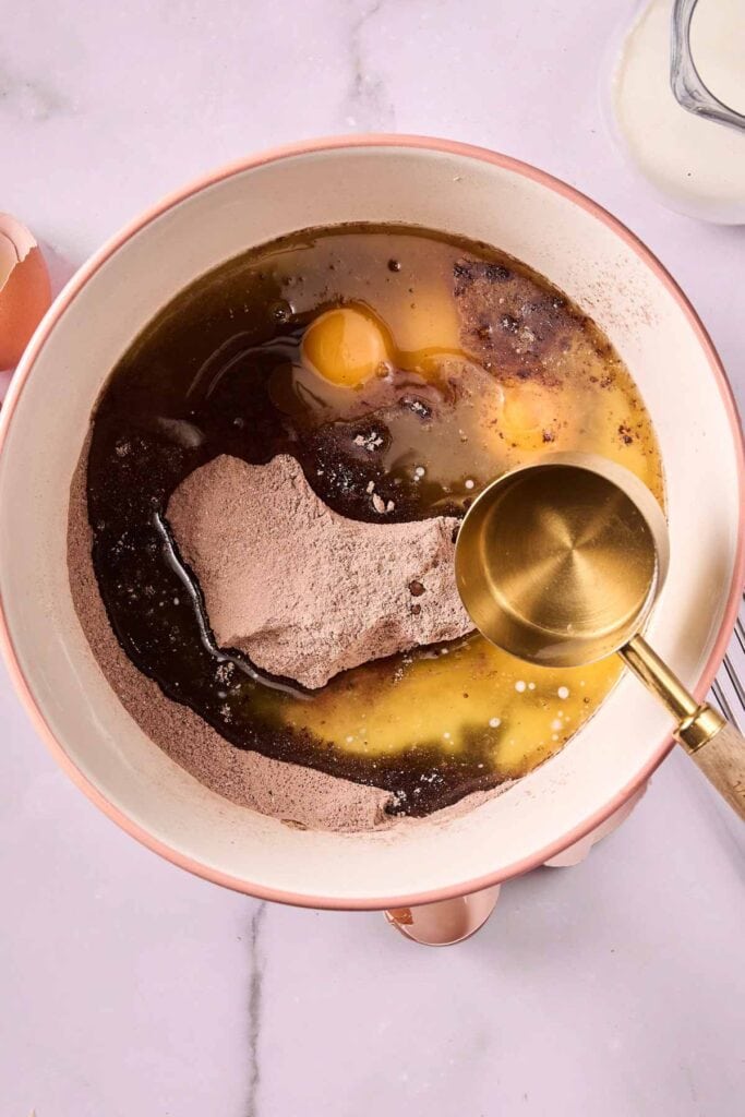 A mixing bowl containing eggs, chocolate cake mix, oil, and water with a measuring cup resting on the edge—perfect for whipping up Banana Pudding Brownies.