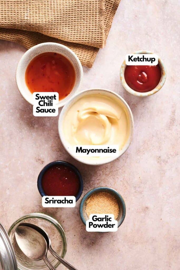 Five small bowls, including a Copycat Savvy Slider sauce, sweet chili sauce, mayonnaise, ketchup, sriracha, and garlic powder, are arranged on a light surface with a brown cloth in the corner.