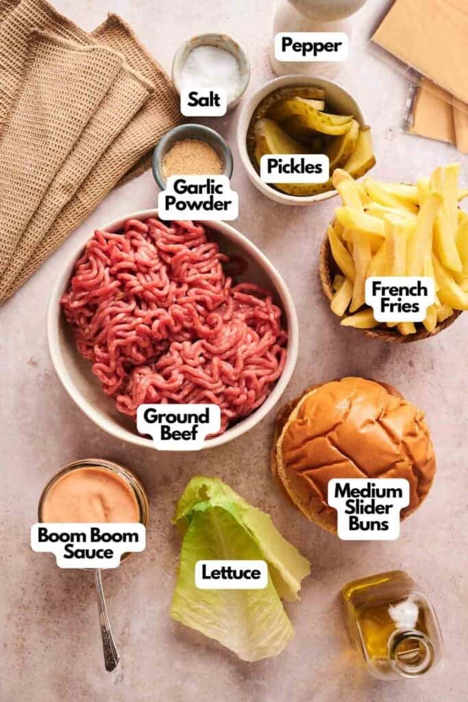 Ingredients for Copycat Savvy Slider sliders laid out on a table, including ground beef, slider buns, lettuce, french fries, pickles, boom boom sauce, garlic powder, salt, and pepper.