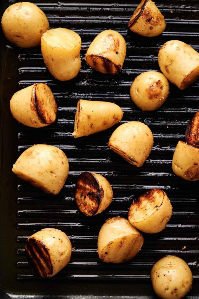 Grilled Potatoes, halved and perfectly seasoned, showcase distinct grill marks as they’re artfully arranged on a black grill pan.