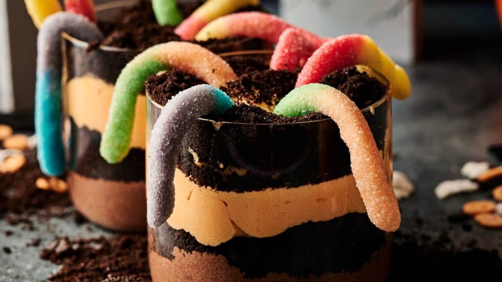Two dessert cups layered with chocolate pudding, crushed cookies, and topped with gummy worms.