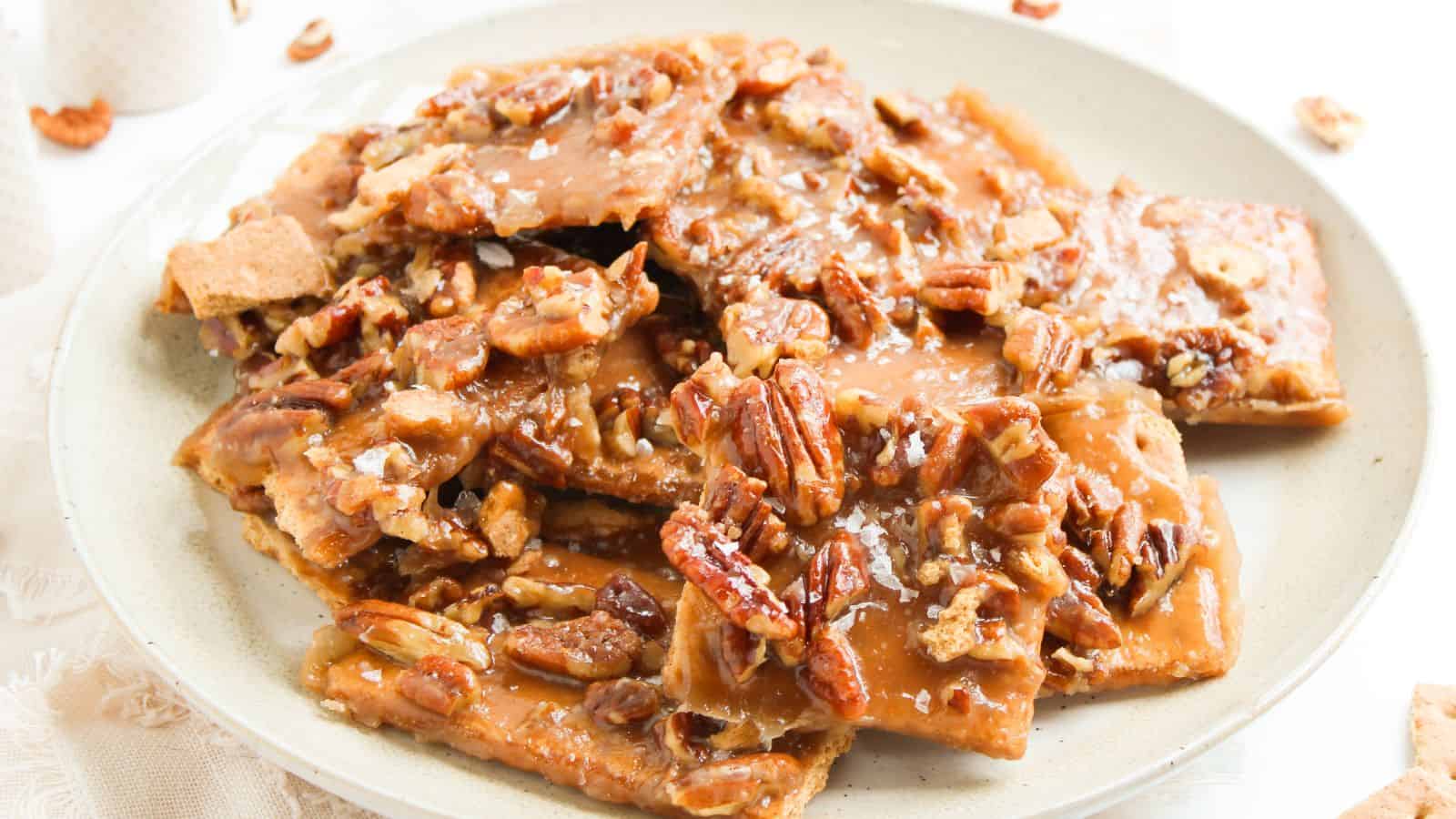 A plate of pecan praline brittle pieces, featuring caramelized sugar and pecans on a light plate.