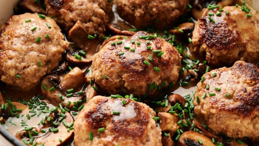 Pan of browned meat patties in a creamy mushroom sauce, garnished with chopped chives.