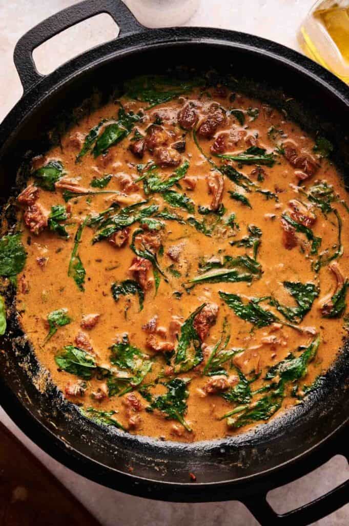 A cast iron skillet filled with creamy sauce, wilted spinach, sun-dried tomatoes, and juicy Marry Me Steak.