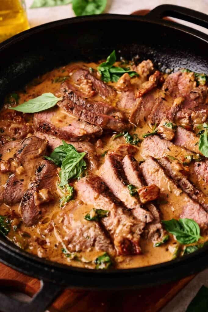 Sliced Marry Me Steak in a creamy sauce with herbs and spinach, served in a black skillet.