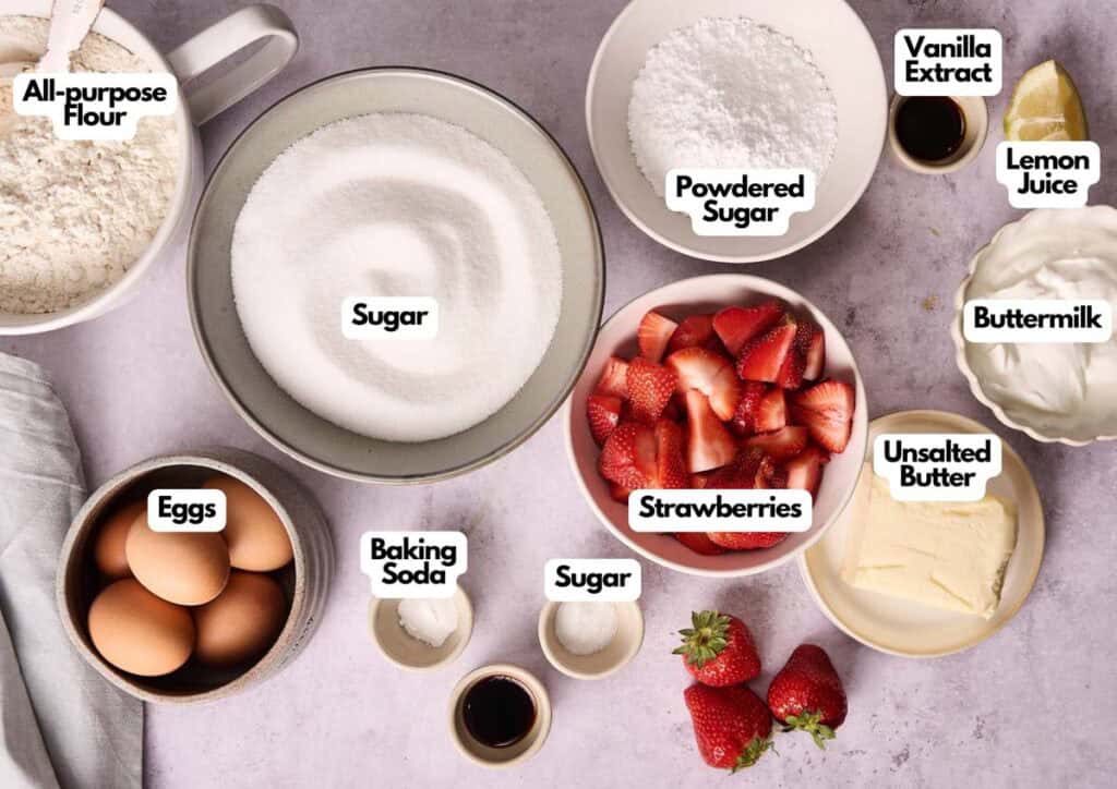 A top-down view of baking ingredients in bowls for Strawberry Pound Cake, including flour, sugar, eggs, baking soda, powdered sugar, vanilla extract, lemon juice, buttermilk, unsalted butter, and strawberries.