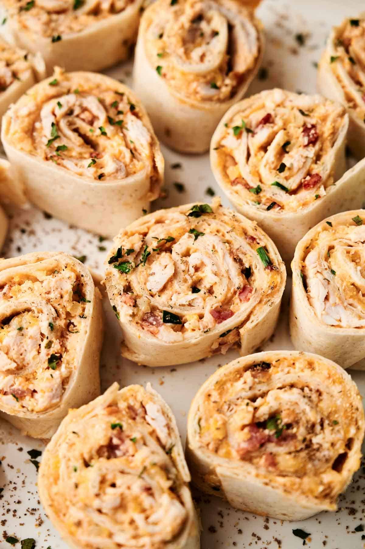 Close-up of several Buffalo Chicken Pinwheels filled with a creamy mixture, shredded chicken, and herbs, arranged on a white surface.