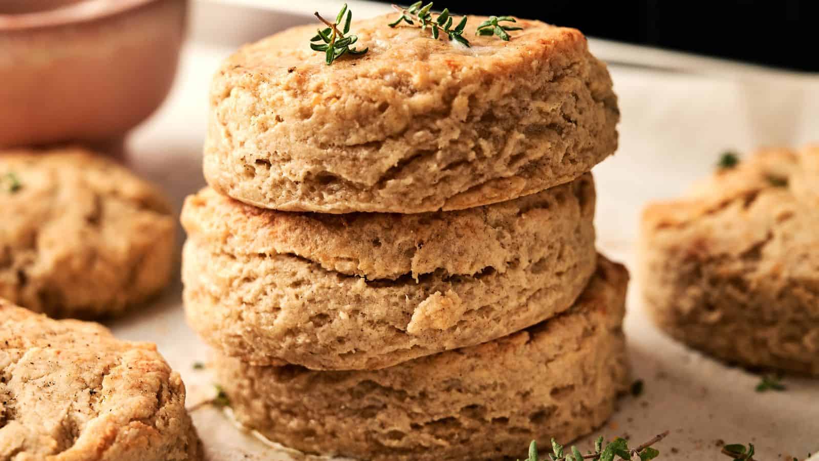 Three golden-brown biscuits stacked on parchment paper, topped with small sprigs of fresh herbs.