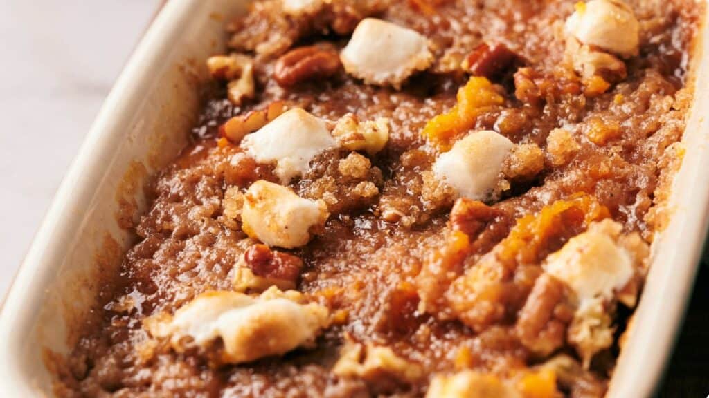 A close-up of a baked sweet potato casserole topped with toasted marshmallows and pecans in a rectangular dish.