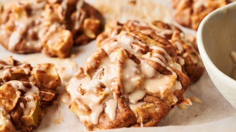 Close-up of freshly baked cookies with chunks of apple and a drizzle of icing, resting on a sheet of parchment paper.